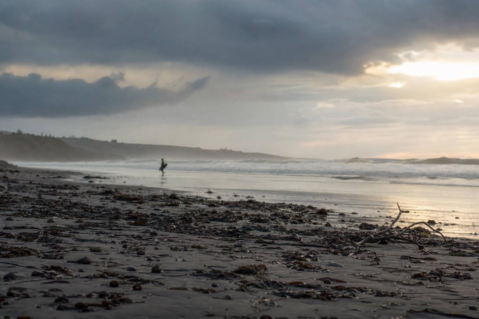 Plage normande juste après une tempête d’hiver : longue houle résiduelle, ciel délavé aux nuages déchirés, algues et bois flotté sur le sable mouillé